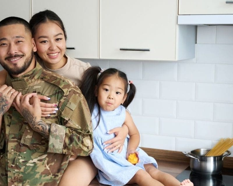 A father in military fatigues with his wife and daughter in their kitchen